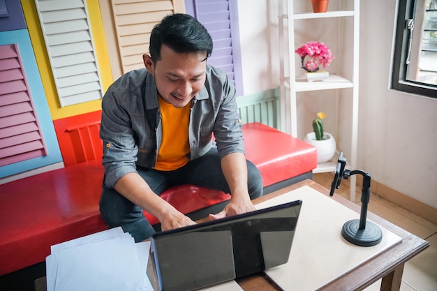 Homme souriant tout en écrivant et en travaillant à l'aide d'un ordinateur portable à la maison