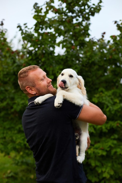 Homme souriant tout en tenant un chiot golden retriever ludique à l'extérieur en été