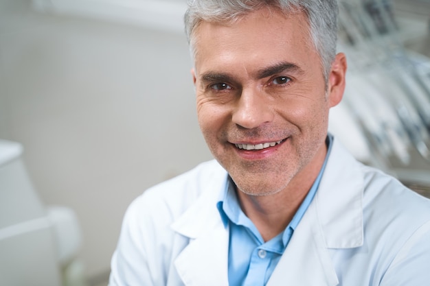 Un homme souriant en uniforme blanc est assis dans un bureau moderne et attend le traitement des patients