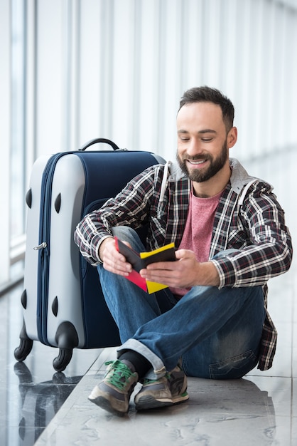 Homme souriant avec une valise et un passeport prêt à voyager.