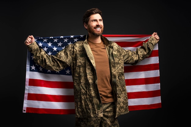 Homme souriant vétéran soldat portant un uniforme de camouflage militaire tenant le drapeau américain isolé