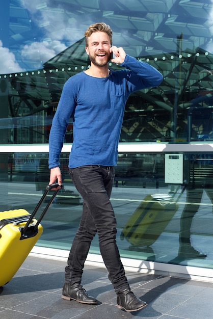 Homme souriant voyageant avec valise et téléphone portable