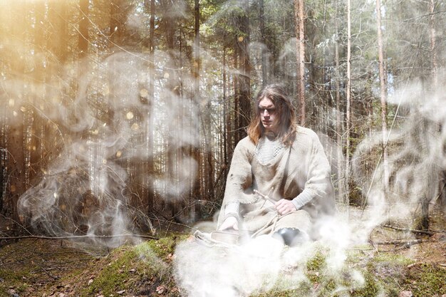 Un homme en soutane passe un rituel dans une forêt sombre avec une boule de cristal et un livre