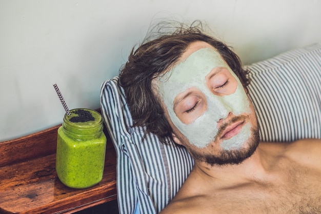 Homme de Spa appliquant un masque d'argile verte pour le visage. Soins de beauté. Smoothie vert frais à la banane et aux épinards au cœur de graines de sésame. L'amour pour un concept d'aliments crus sains. Concept de désintoxication