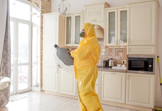 Un homme spécialiste de la lutte contre les insectes dans une combinaison de protection jaune pulvérise les murs de l'appartement