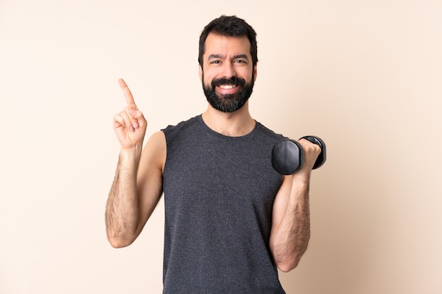 Homme de sport caucasien avec barbe faisant de l'haltérophilie sur un mur isolé heureux et pointant vers le haut