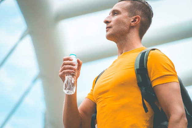 Homme de sport en jaune tient une bouteille d&#39;eau dans la ville moderne
