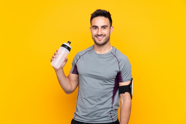 Homme de sport sur mur jaune isolé avec bouteille d'eau de sport