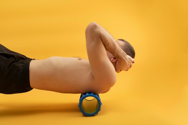 Homme de sport utilisant un rouleau myofascial pour les muscles et le fascia qui s'étendent vers l'arrière. Bel homme faisant des exercices avec un rouleau en mousse. Vue de côté.