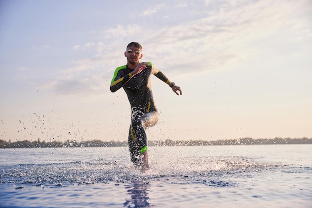 Homme sportif en combinaison et lunettes de formation en triathlète tôt le matin courant dans la rivière