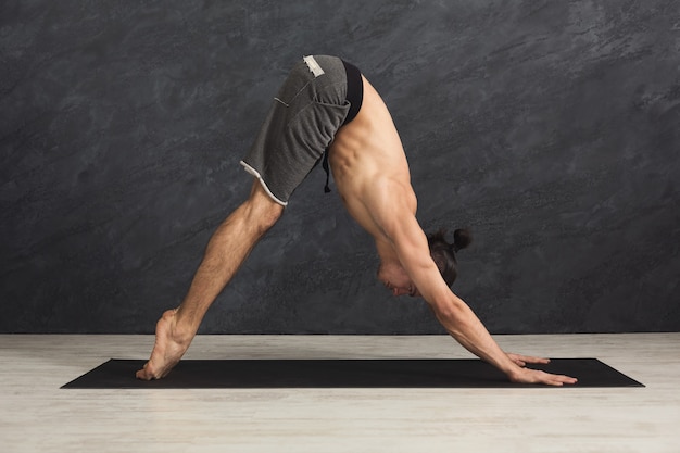 Homme sportif faisant la posture de flexion avant debout. Guy pratiquant le yoga, debout la tête aux genoux au gymnase, espace de copie