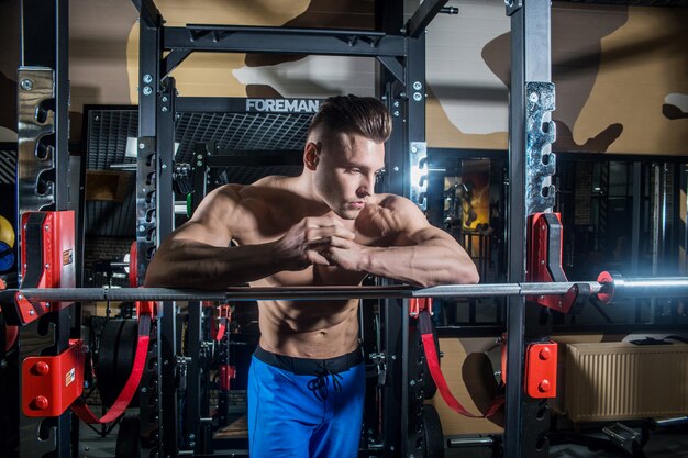 Homme sportif avec de gros muscles et un large dos s'entraîne dans la salle de gym, le fitness et la presse abdominale gonflée