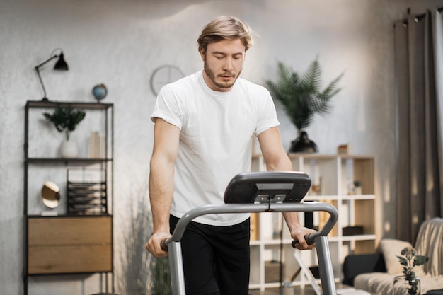 Homme sportif musclé caucasien en t-shirt blanc se pencha ses mains sur le tapis roulant