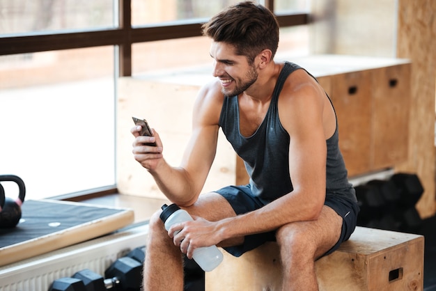 L'homme sportif s'assied sur la boîte et regarde le téléphone portable