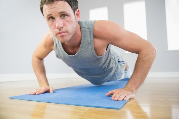 Homme sportif séduisant faire des push ups sur tapis bleu en regardant la caméra