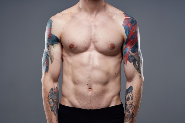Homme sportif avec des tatouages abdominaux gonflés sur ses muscles de fond gris bras