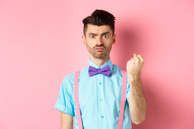 Homme stupide grondant quelqu'un, menaçant la personne avec le poing, l'air grincheux et déçu, debout sur le rose.