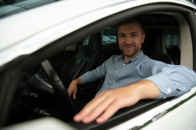 Homme de style et de statut Beau jeune homme en costume complet souriant en conduisant une voiture