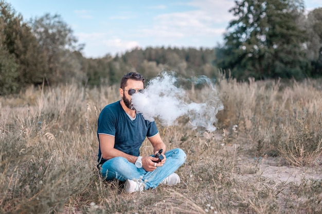 L'homme Stylishvape se repose à l'extérieur et vapote et se défoule d'une e-cigarette. Cigarette électronique.