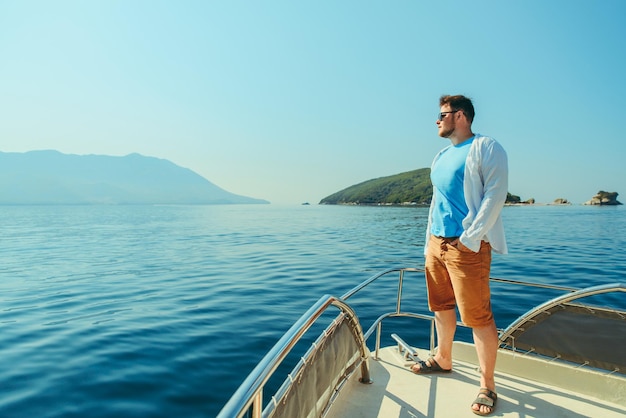 Homme de succès debout au nez du bateau avec mer et montagnes en arrière-plan