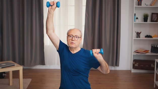 Homme supérieur faisant du sport dans le salon à l'aide d'haltères. Personne âgée retraitée entraînement sain soins de santé sport à la maison, exercice d'activité physique à un âge avancé