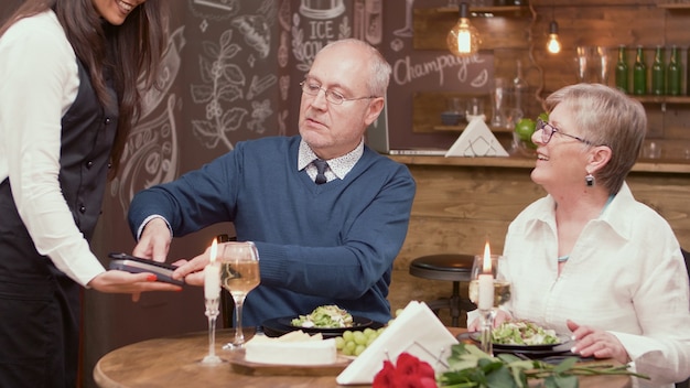 Homme supérieur payant la facture avec sa carte de crédit dans un restaurant. Couple de personnes âgées au restaurant. Vieux couple romantique.