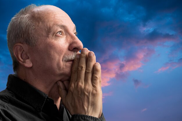 Homme supérieur priant contre le ciel nuageux bleu