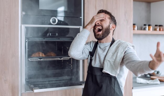 Homme surpris debout près du four avec des croissants brûlés