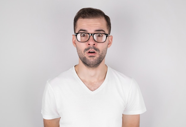 Homme surpris avec des lunettes en t-shirt blanc sur mur gris