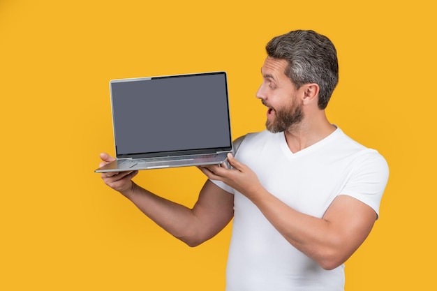 Homme surpris montrant une application isolée sur fond jaune homme montrant une application pour ordinateur portable
