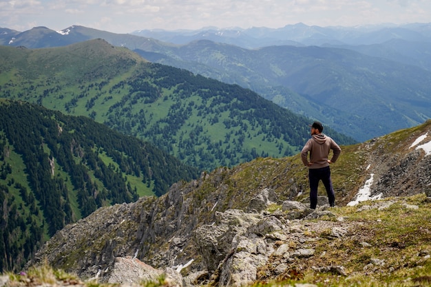 Un homme en sweat à capuche brun se tenant debout sur une pente de montagne devant des montagnes