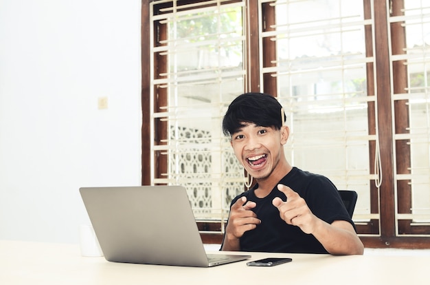 L'homme en t-shirt asiatique noir était assis devant l'ordinateur portable avec une expression très heureuse