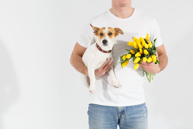 Homme en t-shirt blanc debout avec des fleurs et un chien.