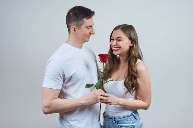 Un homme en T-shirt blanc donne une rose rouge à une blonde semeuse