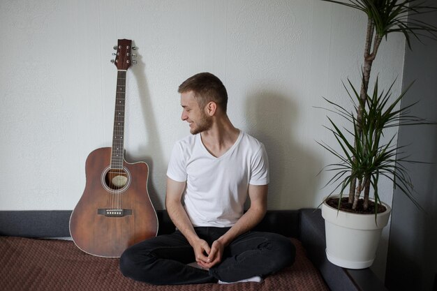 Un homme en t-shirt blanc est assis avec une guitare