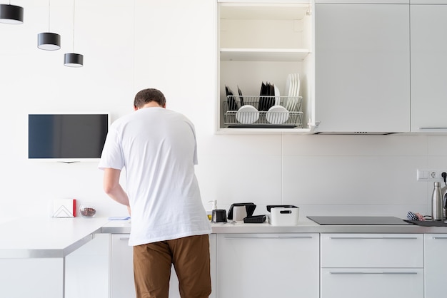 Homme en t-shirt blanc laver la vaisselle dans la cuisine