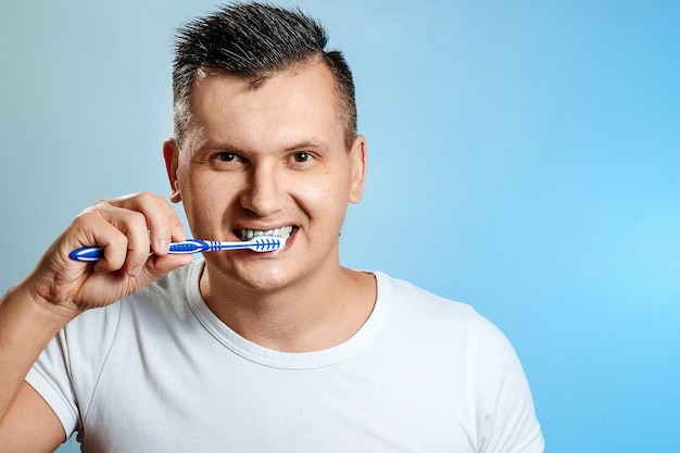 Un homme en t-shirt blanc se brosse les dents en bleu