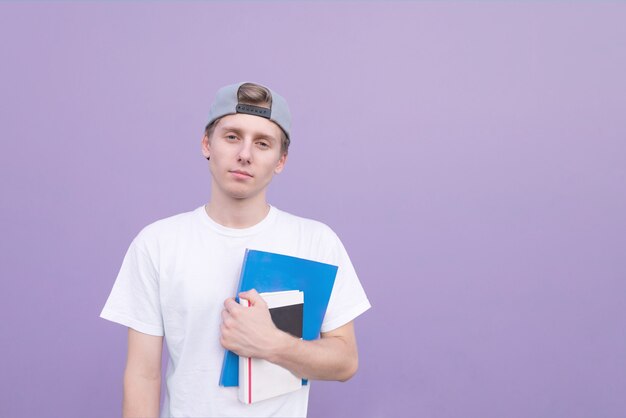 Homme en T-shirt blanc se dresse sur un fond violet avec des livres et des cahiers