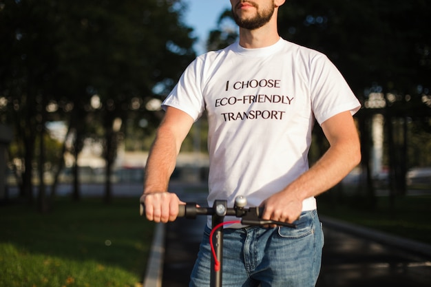 Un homme en t-shirt blanc tient les bras de son scooter électrique alors qu'il circule dans un parc, surface floue