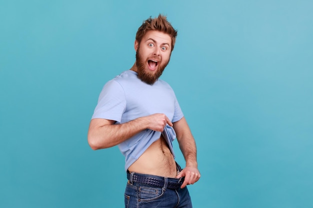 Homme en T-shirt bleu ayant des points de volonté à la taille fine dans un gros pantalon perte de poids réussie