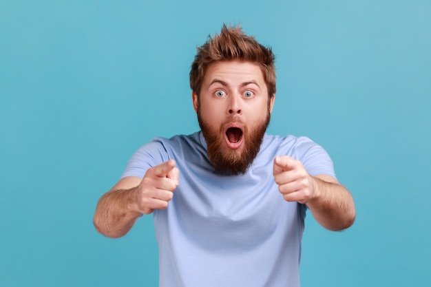 L'homme en T-shirt bleu pointe les doigts regarde la caméra avec la bouche ouverte et de grands yeux choqués par le choix