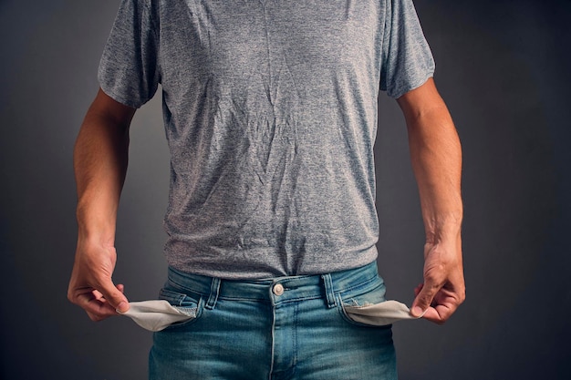 Un homme en T-shirt gris froissé et en jean avec les poches vides Concept de faillite et de pauvreté