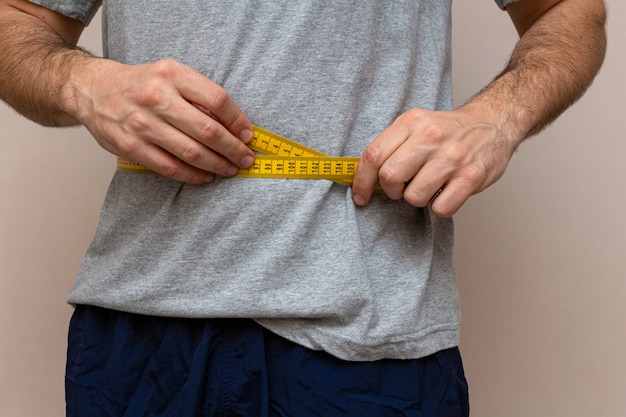 Un homme en T-shirt gris mesure la taille avec un ruban jaune