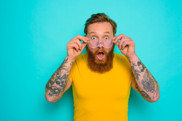 Un homme avec un t-shirt jaune et une barbe est choqué par quelque chose