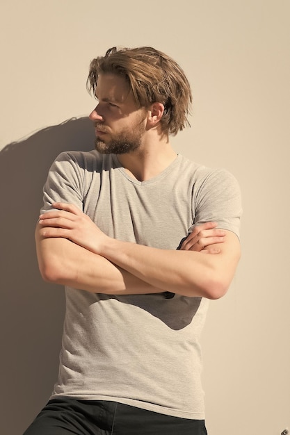 Homme en t-shirt pose avec les mains jointes sur le mur gris