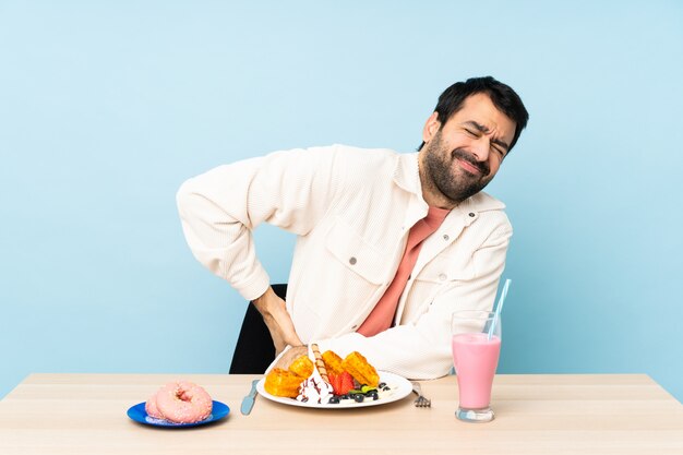 Homme à une table ayant des gaufres et un milkshake souffrant de maux de dos pour avoir fait un effort