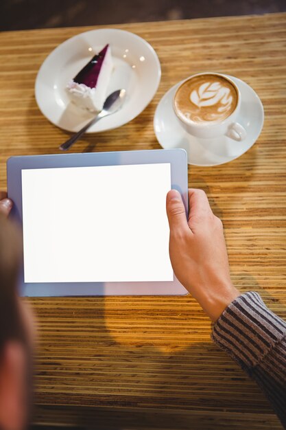 Homme avec une tablette ayant un cappuccino et un gâteau