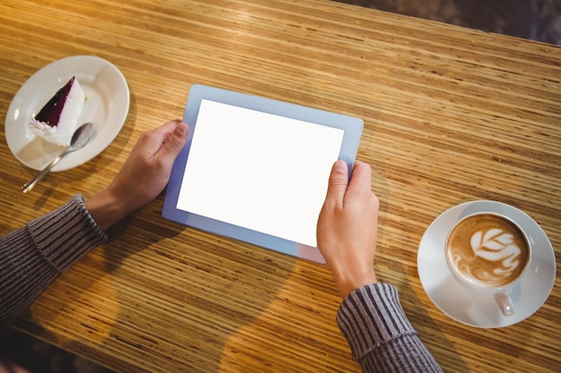 Homme avec une tablette ayant un cappuccino et un gâteau