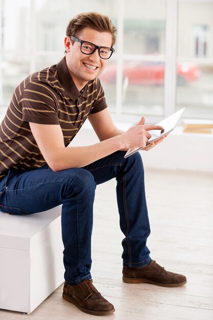 Homme avec tablette numérique. Vue latérale du beau jeune homme travaillant sur tablette numérique et regardant la caméra