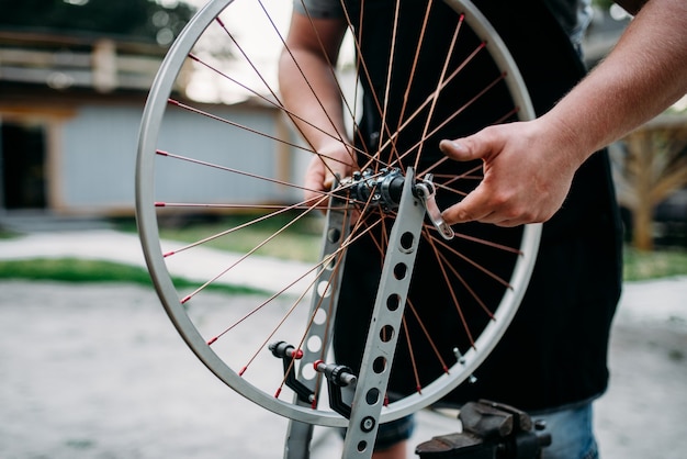 Un homme en tablier ajuste les rayons et la roue du vélo avec des outils de service.